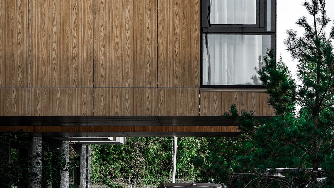 Husfasad med stående träpanel, fönster och carport under utskjutande våning